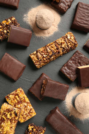 Different tasty energy bars and protein powder on black table, flat lay