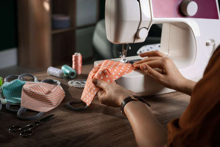 Woman sewing cloth protective mask with machine at table indoors, closeupの写真素材
