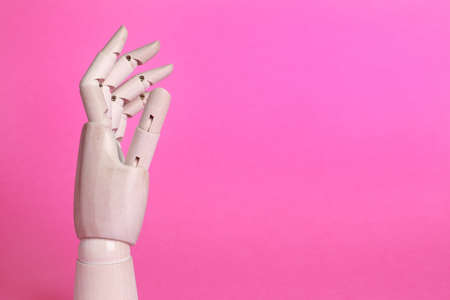 Wooden mannequin hand on pink background. Space for textの写真素材