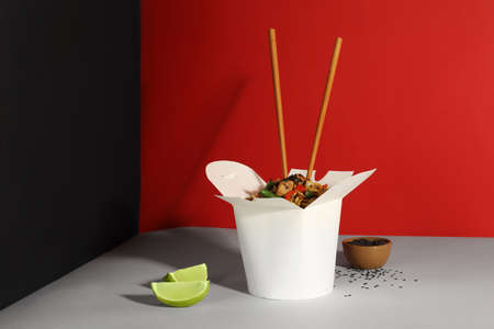 Box of wok noodles with vegetables, meat and chopsticks on color backgroundの写真素材