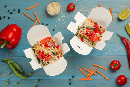 Boxes of vegetarian wok noodles with ingredients on light blue wooden table, flat layの写真素材