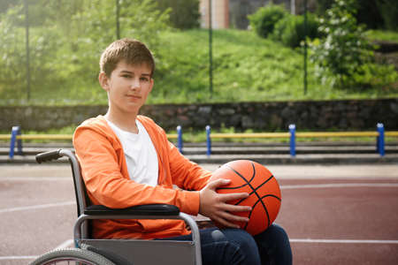 Disabled teenage boy in wheelchair with basketball ball at outdoor courtの写真素材
