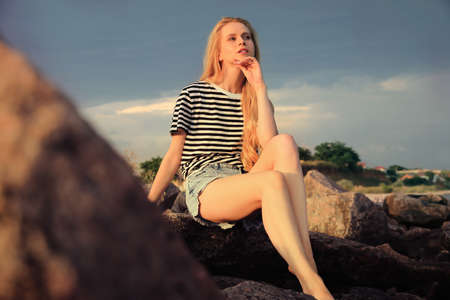 Beautiful young woman sitting on rocks outdoorsの写真素材