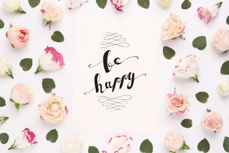 Frame of beautiful flowers and paper card with handwritten text Be happy on white background, flat layの写真素材
