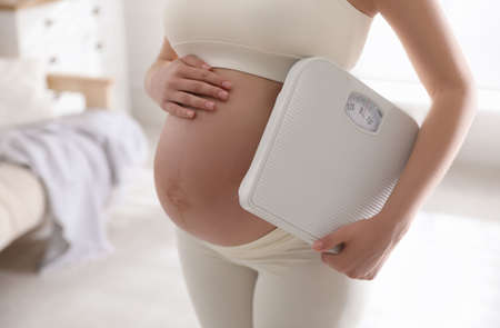 Young pregnant woman with scales at home, closeupの写真素材