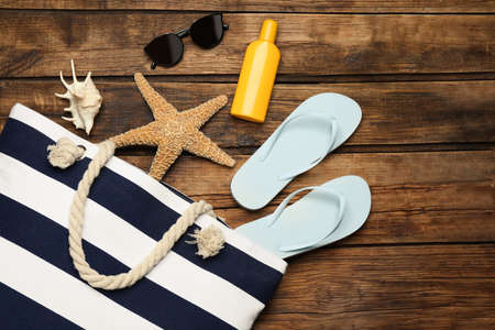 Stylish bag and beach accessories on wooden background, flat lay