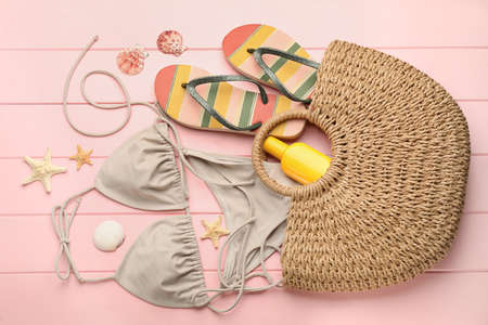 Stylish bag and beach accessories on pink wooden background, flat lay