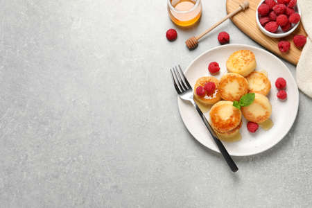 Delicious cottage cheese pancakes with raspberries and honey on light gray table, flat lay. Space for textの写真素材