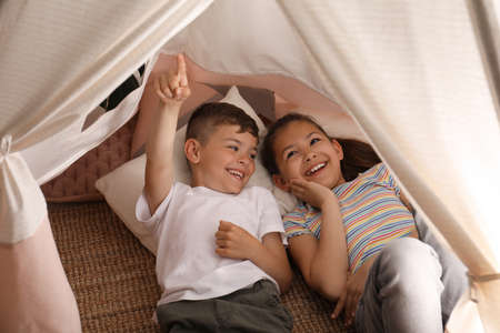 Cute little children lying in toy wigwam at homeの写真素材