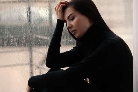 Depressed woman near window on rainy dayの写真素材