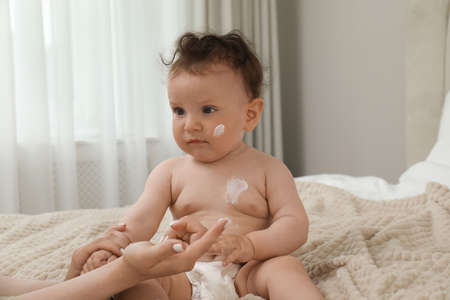 Mother applying body cream on her baby in bedroomの写真素材