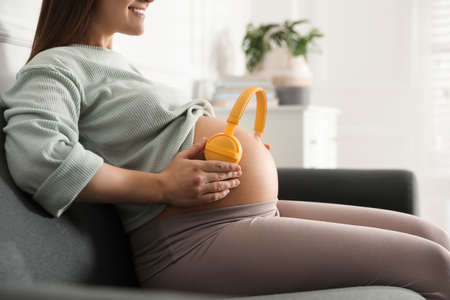 Pregnant woman with headphones on her belly at home, closeup