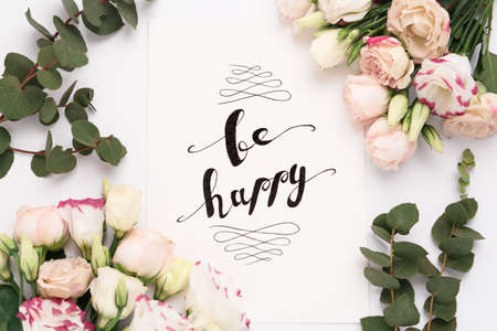 Frame of beautiful flowers and paper card with handwritten text Be happy on white background, flat layの写真素材