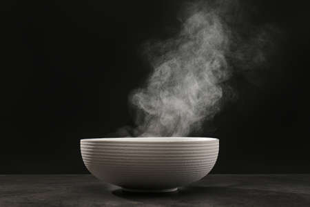 Steaming ceramic bowl on gray table against dark backgroundの写真素材