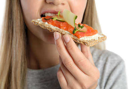 Woman eating fresh rye crispbread with cream cheese, salmon and cucumber on white background, closeupの写真素材