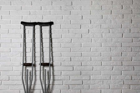 Pair of axillary crutches near white brick wall. Space for textの写真素材