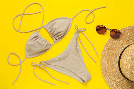 Stylish beige bikini, sunglasses and hat on yellow background, flat layの写真素材