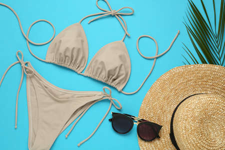 Stylish beige bikini, sunglasses and hat on light blue background, flat layの写真素材