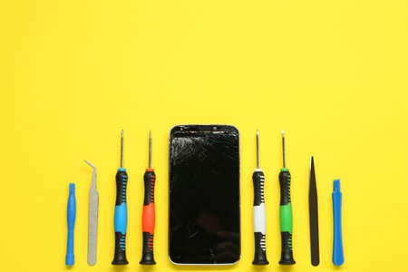 Damaged smartphone and repair tool set on yellow background, flat lay. Space for textの写真素材