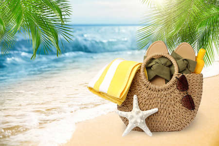 Stylish bag with different accessories on tropical sandy beach, space for text