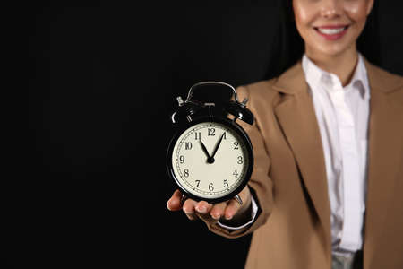 Businesswoman holding alarm clock on black background, closeup with space for text. Time managementの写真素材