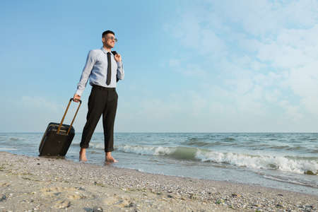 Happy businessman with suitcase walking on beach. Business tripの写真素材