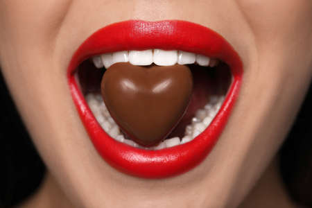 Young woman with red lips eating heart shaped chocolate candy, closeupの写真素材