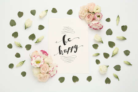 Frame of beautiful flowers and paper card with handwritten text Be happy on white background, flat layの写真素材