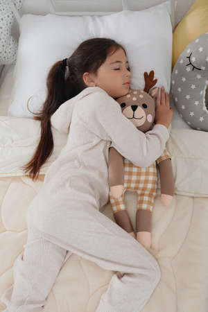 Cute girl in pajamas sleeping with toy deer at homeの写真素材