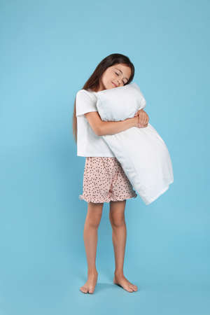 Cute girl wearing pajamas with pillow on light blue backgroundの写真素材