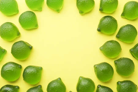 Frame of delicious gummy lime candies on green background, flat lay. Space for text