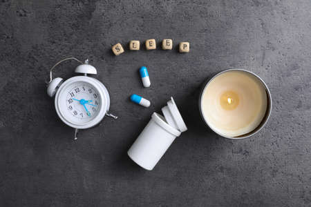 Word Sleep made of wooden cubes near alarm clock, candle and pills on gray background, flat lay. Insomnia treatmentの写真素材