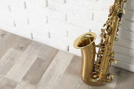 Beautiful saxophone on floor near white brick wall indoors, closeup. Space for textの写真素材