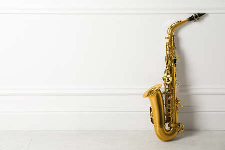 Beautiful saxophone on floor near white wall indoors, space for textの写真素材
