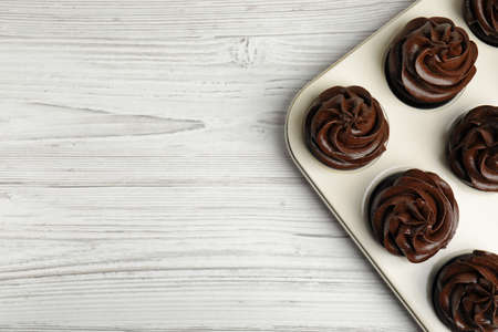 Delicious chocolate cupcakes with cream in baking tray on white wooden table, top view. Space for textの写真素材