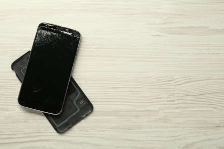 Damaged smartphone on wooden background, flat lay with space for text. Device repairingの写真素材