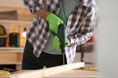 Carpenter working with electric drill at table indoors, closeupの写真素材