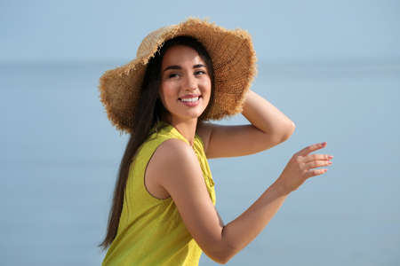 Beautiful young woman wearing straw hat on blurred background. Stylish headdress