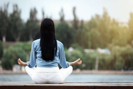Young woman meditating near river, back view. Space for textの写真素材