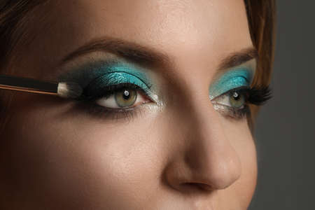 Applying eye shadow onto woman's face on gray background, closeup. Beautiful evening makeup