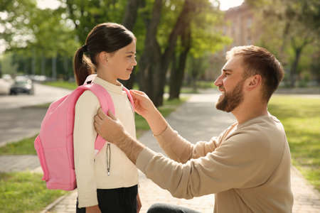 Happy father helping little daughter to put on schoolbag outdoorsの写真素材