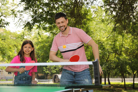 Happy man with his daughter playing table tennis in parkの写真素材