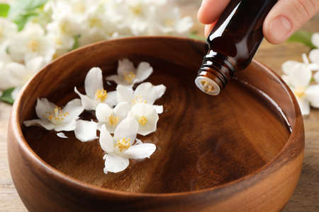 Woman dripping jasmine essential oil into wooden bowl on table, closeupの写真素材