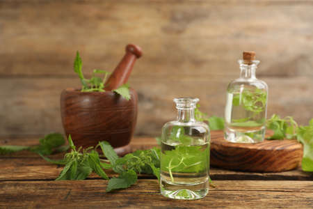 Stinging nettle extract and leaves on wooden background. Natural hair care