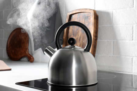 Steaming kettle on electric stove in kitchenの写真素材