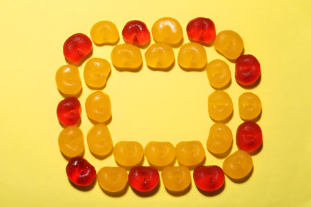 Frame of delicious gummy cherry candies on yellow background, flat lay. Space for textの写真素材