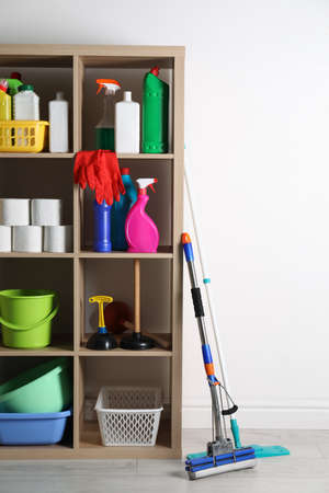 Shelving unit with detergents, cleaning tools and toilet paper near white wall indoorsの写真素材