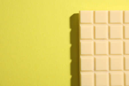 Delicious white chocolate bar on yellow background, top view. Space for text