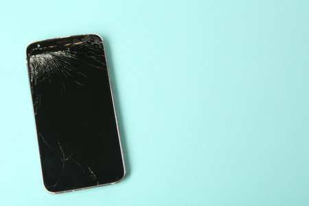 Top view of smartphone with cracked screen on light blue background, space for text. Device repairの写真素材