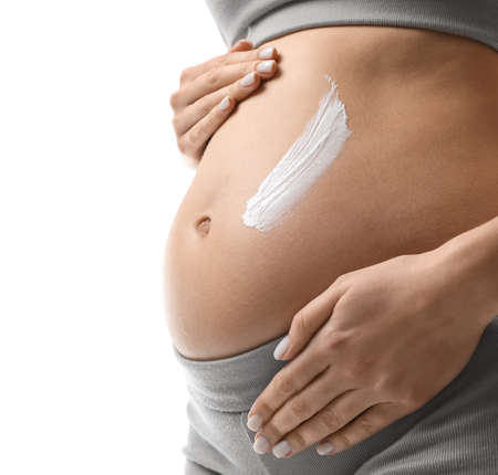 Pregnant woman applying cosmetic product on belly against white background, closeupの写真素材